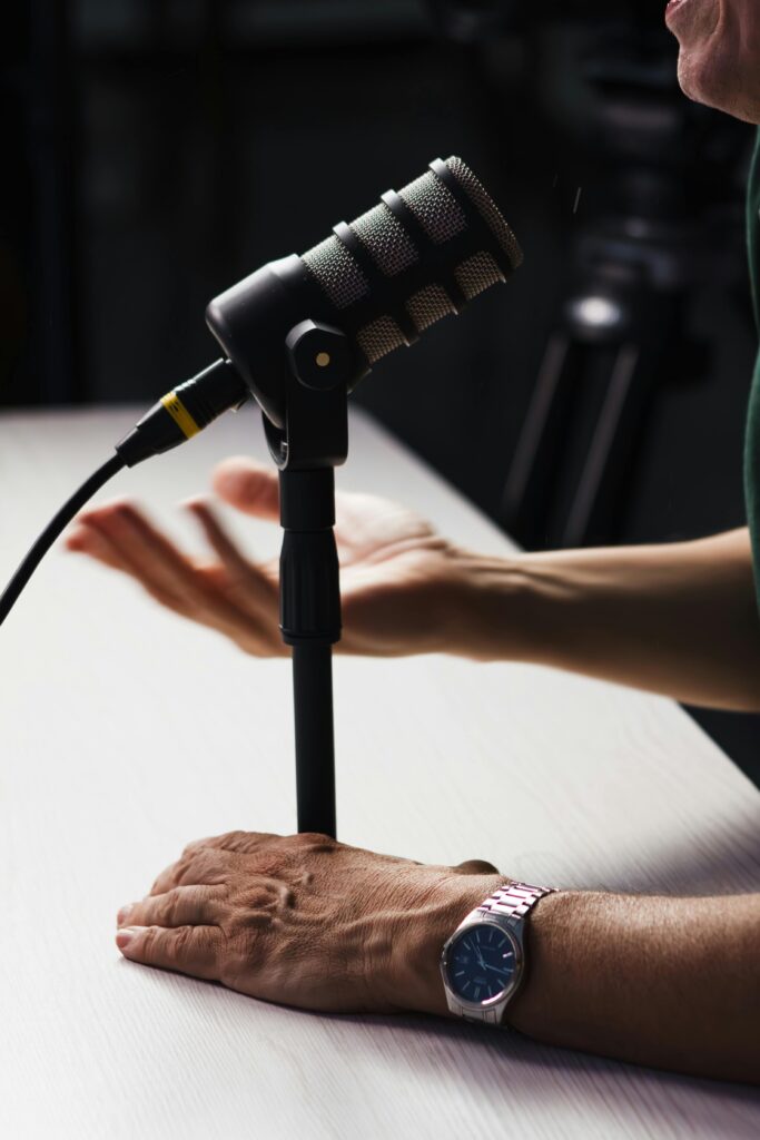 A microphone setup in a podcast studio environment with visible hands, indicating recording session.